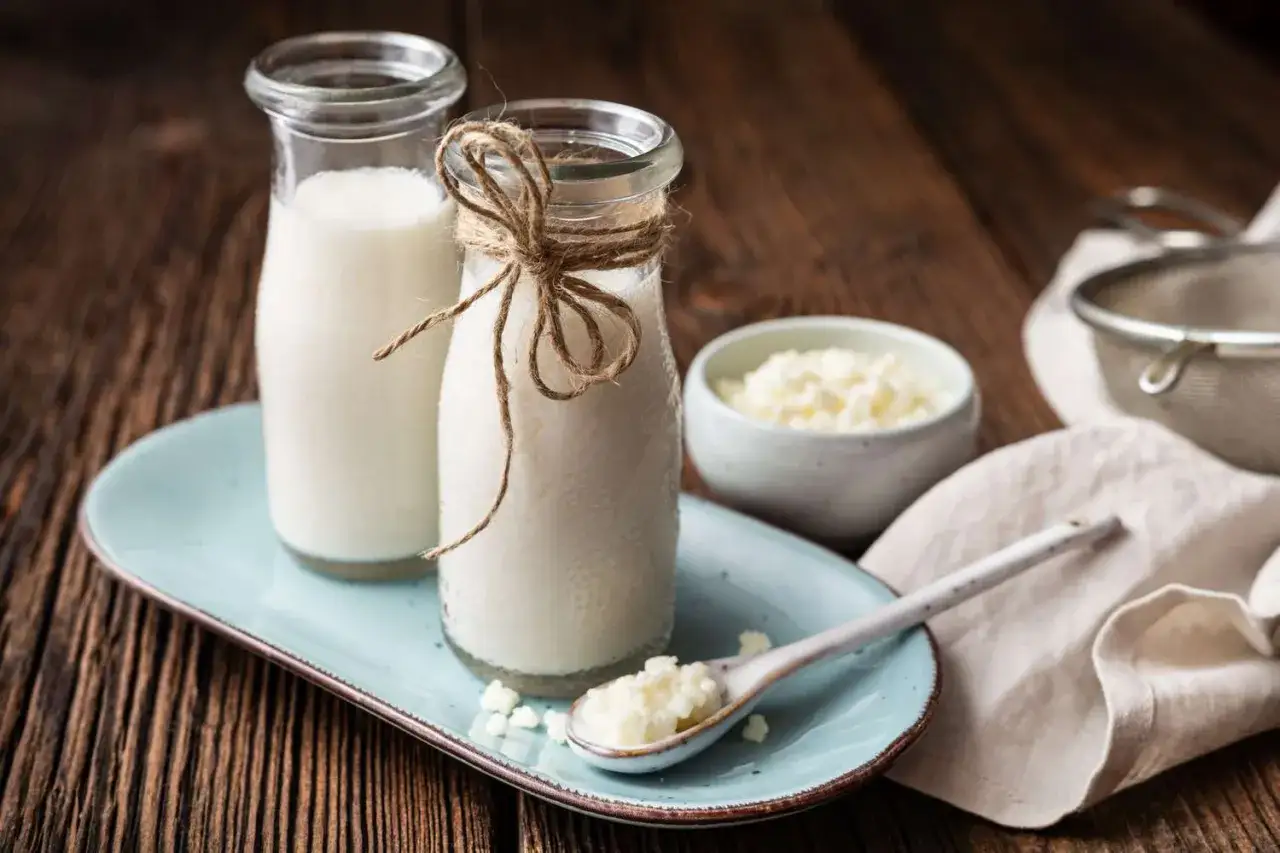 Deux bouteilles de lait, une cuill&egrave;re et un bol de grains de k&eacute;fir sur un plateau bleu. Le k&eacute;fir, une boisson ferment&eacute;e, est pr&ecirc;t &agrave; &ecirc;tre d&eacute;gust&eacute;.