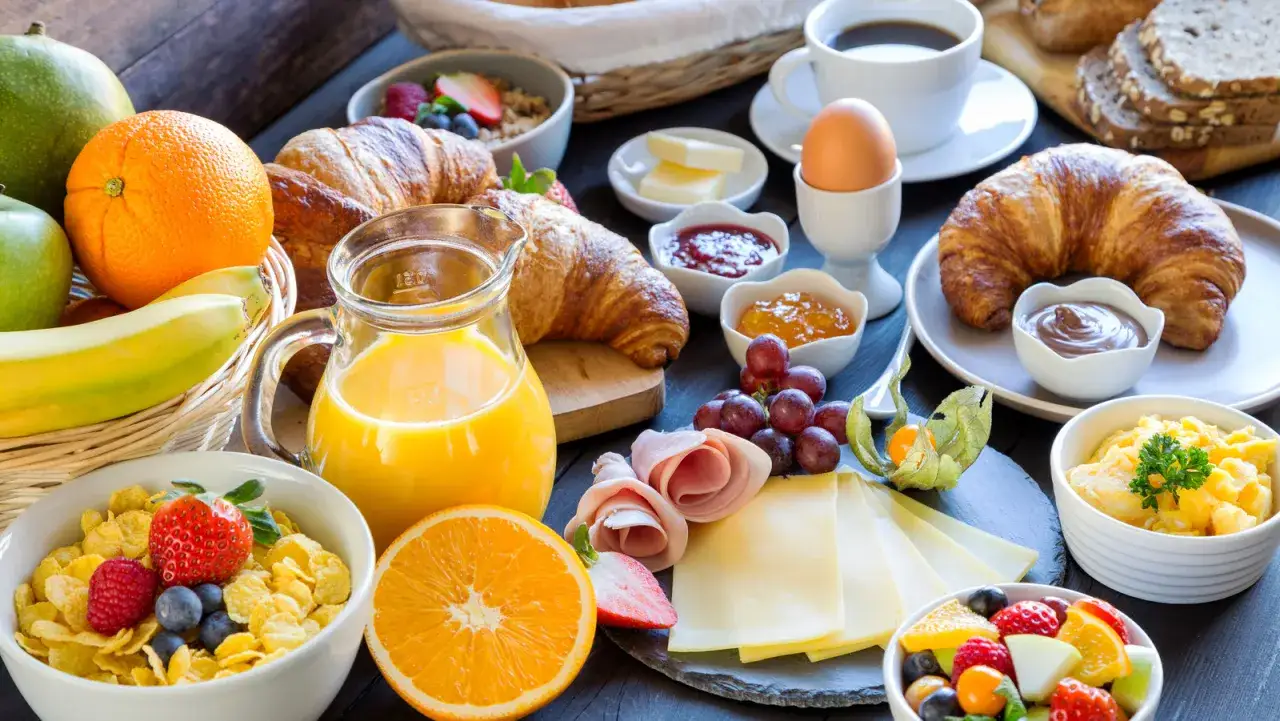 Petit-d&eacute;jeuner copieux avec croissants, jus d'orange, fruits frais et &oelig;ufs. Id&eacute;al pour savoir quel th&eacute; boire le matin pour accompagner ce festin.