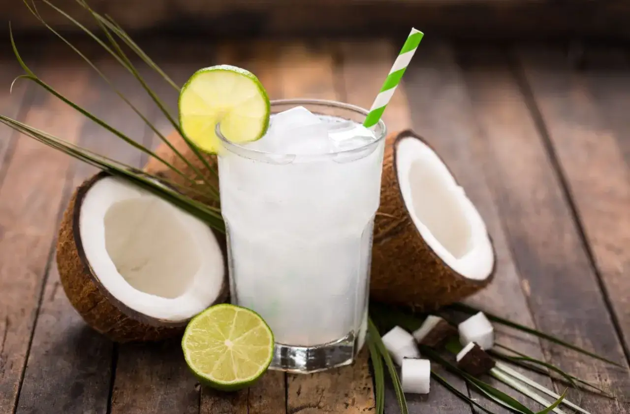 Verre de boisson rafra&icirc;chissante &agrave; l'eau de coco, garni de citron vert et de feuilles de palmier. Une id&eacute;e de recette avec eau de coco.