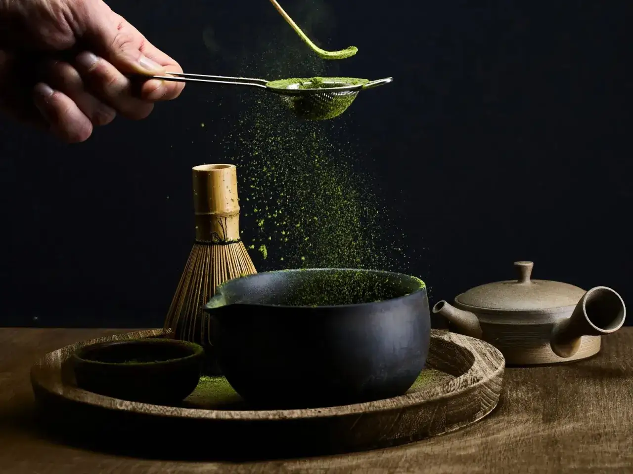 Préparation d'un thé matcha antioxydant : poudre verte tamisée dans un bol, avec un fouet en bambou et une théière.