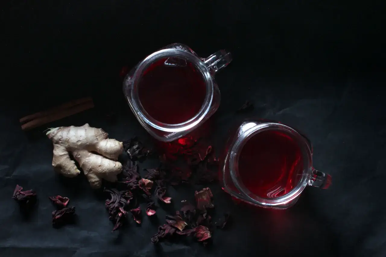 Deux verres de bissap chaud, accompagnés de gingembre et de bâtons de cannelle, sur fond sombre.
