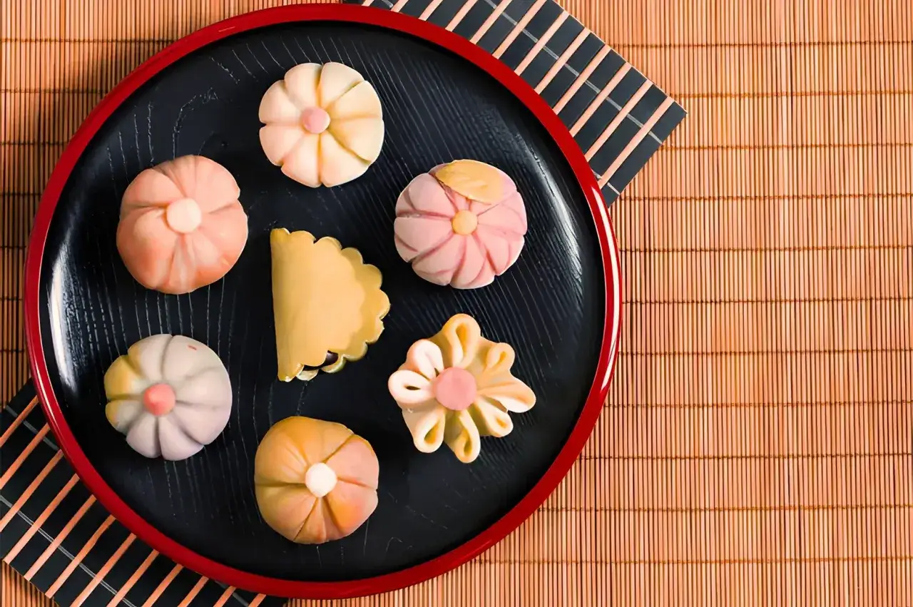 Un plateau noir pr&eacute;sente un assortiment de wagashi, un dessert japonais traditionnel aux formes florales et aux couleurs pastel.