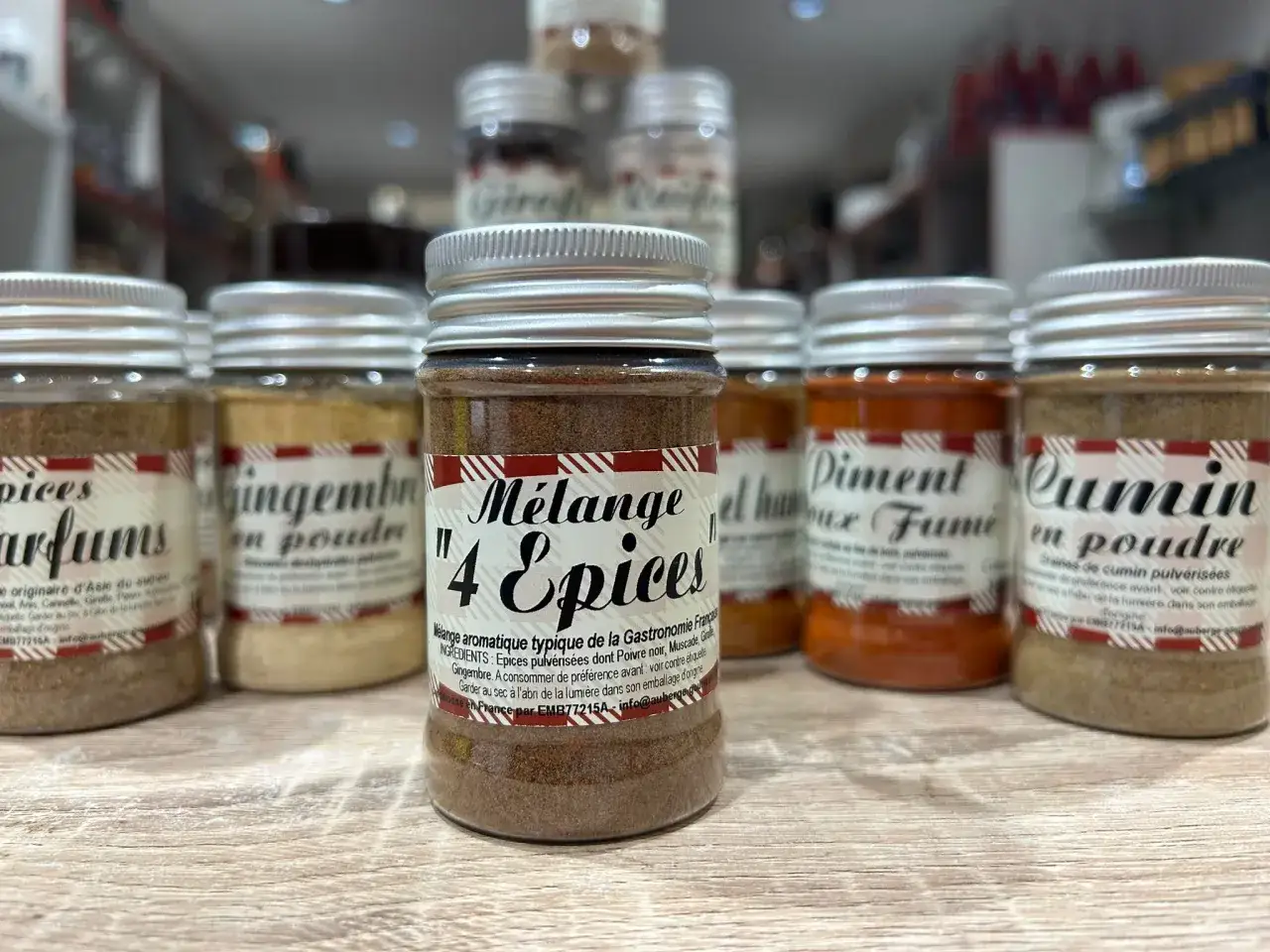 Un pot de mélange 4 épices, typique de la gastronomie française, se trouve au centre d'une étagère remplie d'autres épices en poudre.