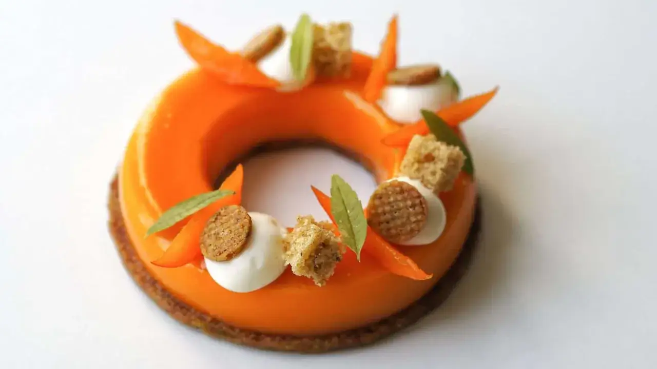 Un entremet abricot, rond et glac&eacute;, d&eacute;cor&eacute; de fruits confits, de cr&egrave;me, de biscuits et de feuilles vertes.