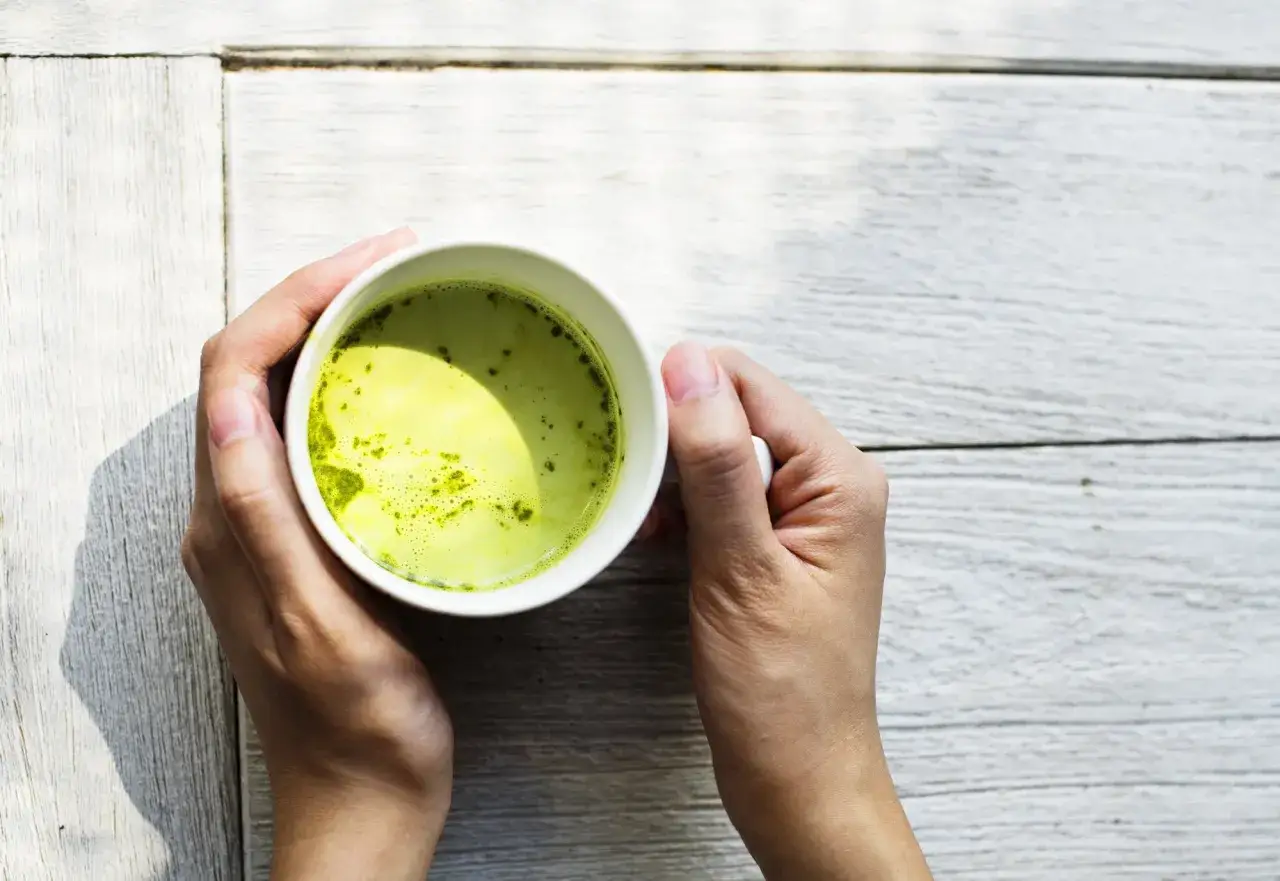Deux mains tiennent une tasse de matcha, une boisson verte vibrante, parfaite pour un coup de pouce de matcha cafeine.