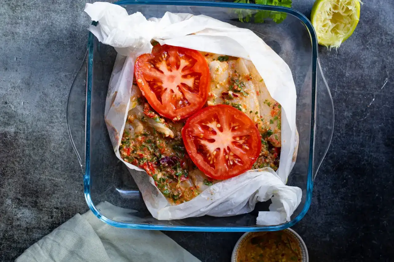 Poisson en papillote prêt à cuire, garni de rondelles de tomate et d'herbes fraîches. Un plat sain et savoureux.