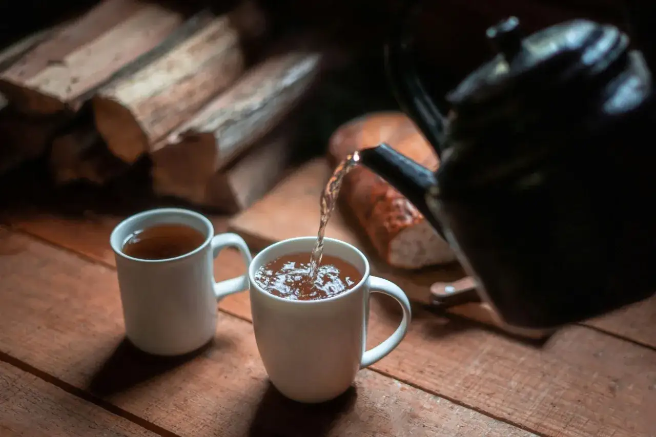 Un thé noir le soir, versé dans une tasse blanche, avec du bois de chauffage en arrière-plan.