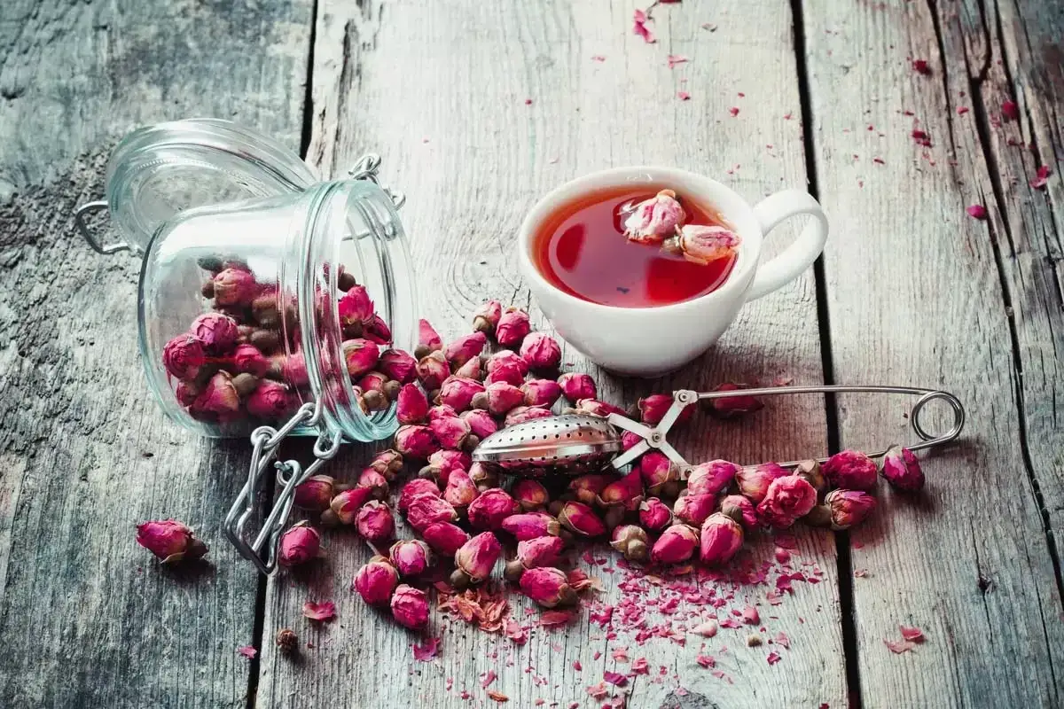 Une tasse de th&eacute; sans th&eacute;ine aux boutons de rose, un pot en verre renvers&eacute; et des p&eacute;tales &eacute;parpill&eacute;s sur un bois vieilli.