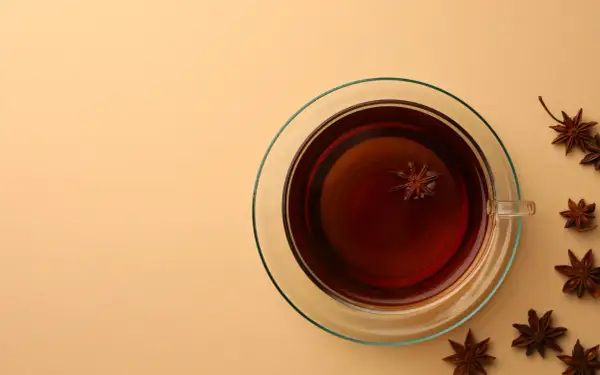 Une tasse de thé ambré avec une étoile d'anis flottant à l'intérieur. Autour, plusieurs étoiles d'anis, rappelant le danger potentiel de l'anis étoilé japonais.