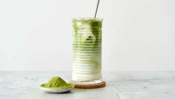 Un verre de matcha frappé, crémeux et rafraîchissant, avec une cuillère de poudre de matcha à côté.