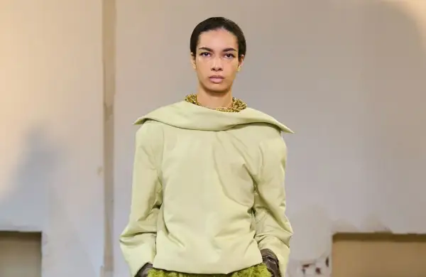 Mannequin portant un haut ample couleur matcha, avec un collier doré audacieux et une jupe texturée verte.
