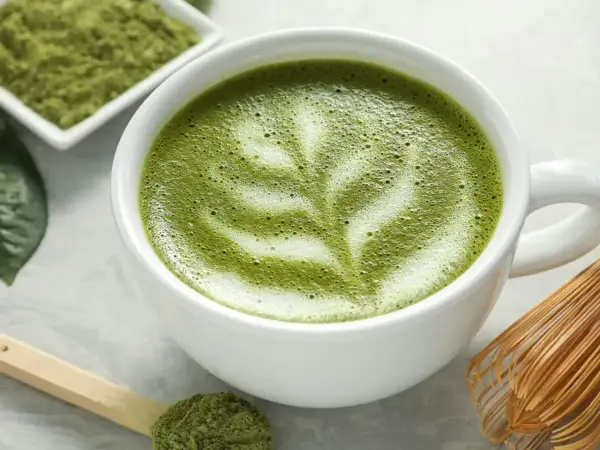 Un délicieux café matcha latte, orné d'une mousse crémeuse et d'une pincée de poudre de matcha sur une cuillère en bois.