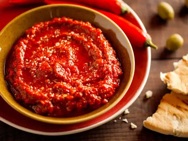 Un bol de harissa maison, prêt à être dégusté avec du pain pita. Une recette simple pour un goût authentique.