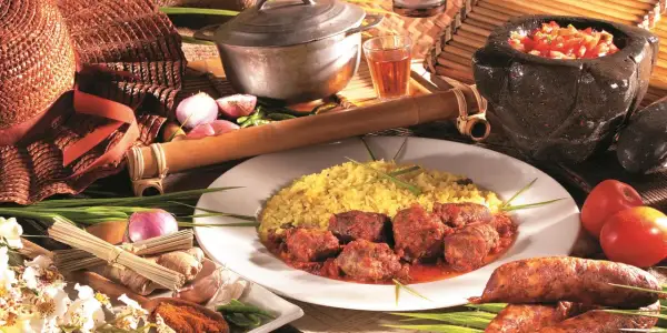 Un rougail saucisses traditionnel, servi avec du riz jaune, des tomates, des oignons et des épices.