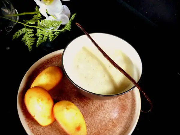 Un bol de lait vanille onctueux, garni d'une gousse de vanille, avec des madeleines dorées sur une assiette.