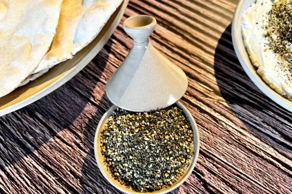 Un bol de zaatar prêt à être utilisé pour une recette, avec du pain pita et une trempette crémeuse.