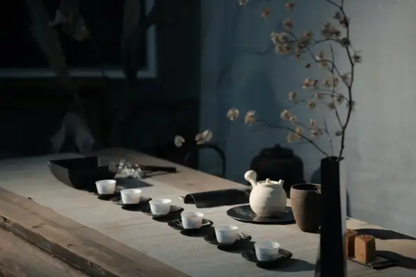 Service à thé minimaliste avec tasses blanches alignées. Une théière en céramique et un vase de fleurs séchées évoquent l'art de comment conserver le thé.