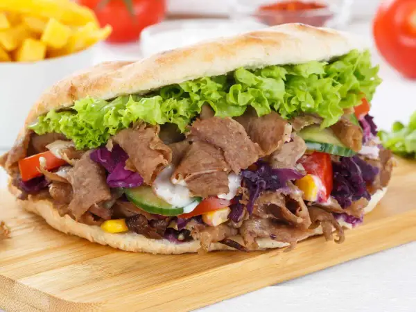 Un généreux kebab maison garni de viande, salade, tomates, concombre et chou rouge, prêt à être dégusté.