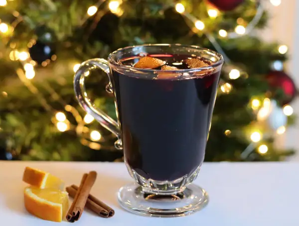 Verre de vin chaud sans alcool, garni d'orange et de cannelle, devant un sapin de Noël illuminé. Parfait pour une recette festive et réconfortante.