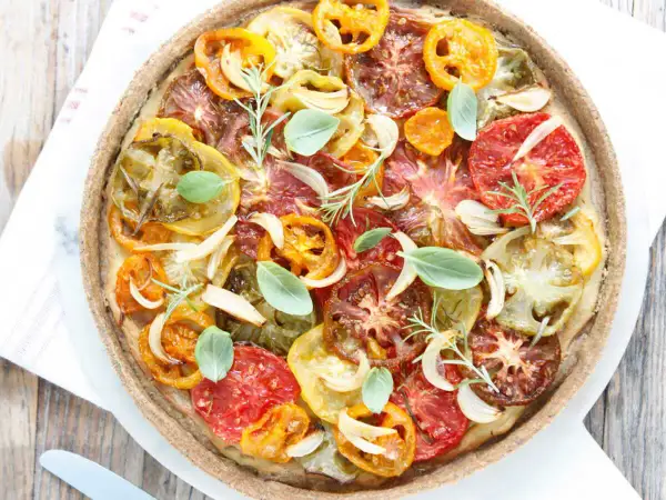 Tarte tomate claire au matcha, garnie de tomates multicolores, oignons, ail, romarin et basilic frais. Une œuvre culinaire colorée et savoureuse.